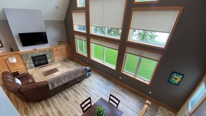 Ein großzügiges Wohnzimmer mit einer großen Eckcouch, einem Kamin und mehreren Fenstern mit Blick ins Freie.