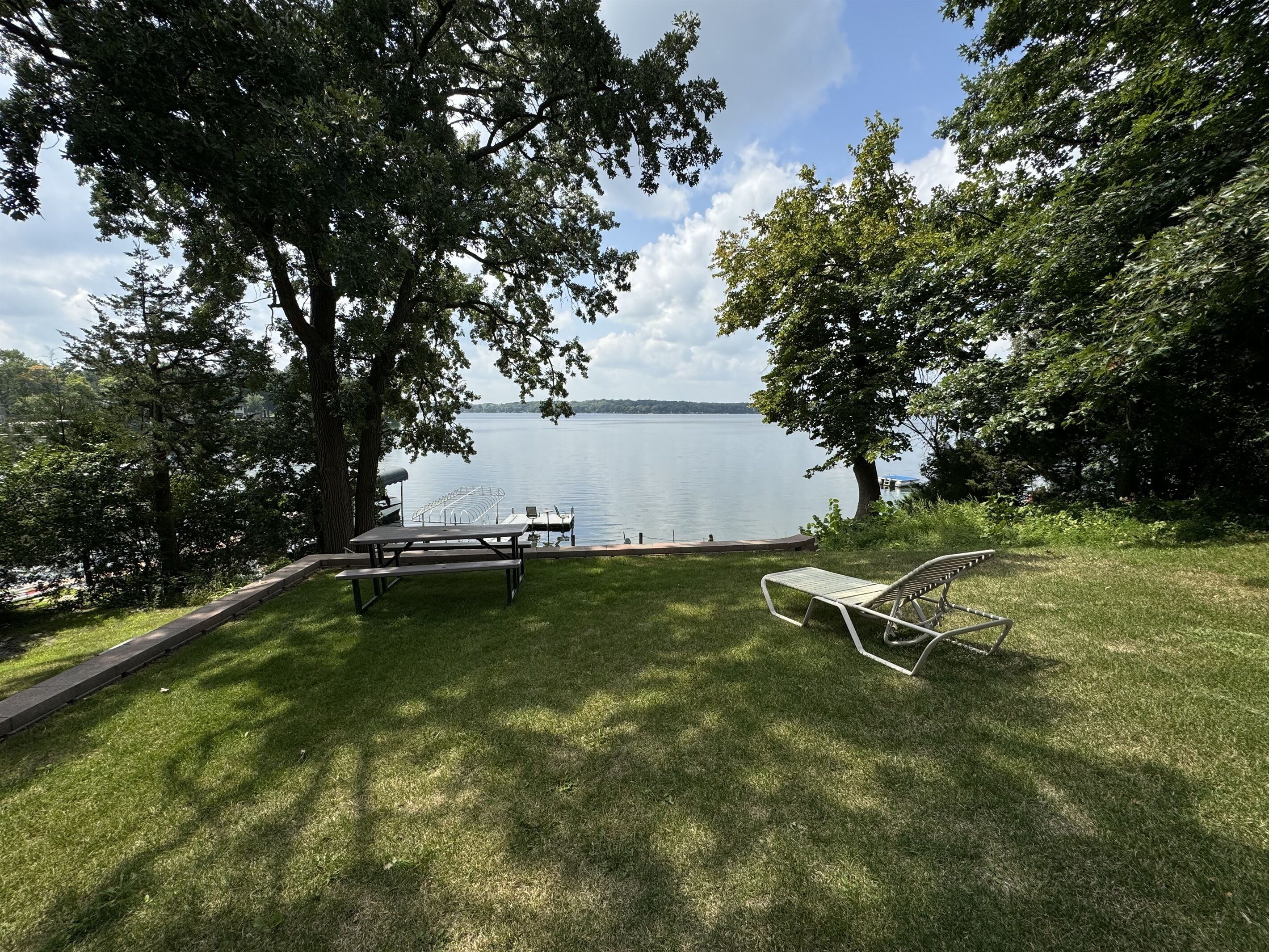 Een picknickplaats aan het meer met een tafel en stoelen, omringd door bomen en uitzicht op het water.
