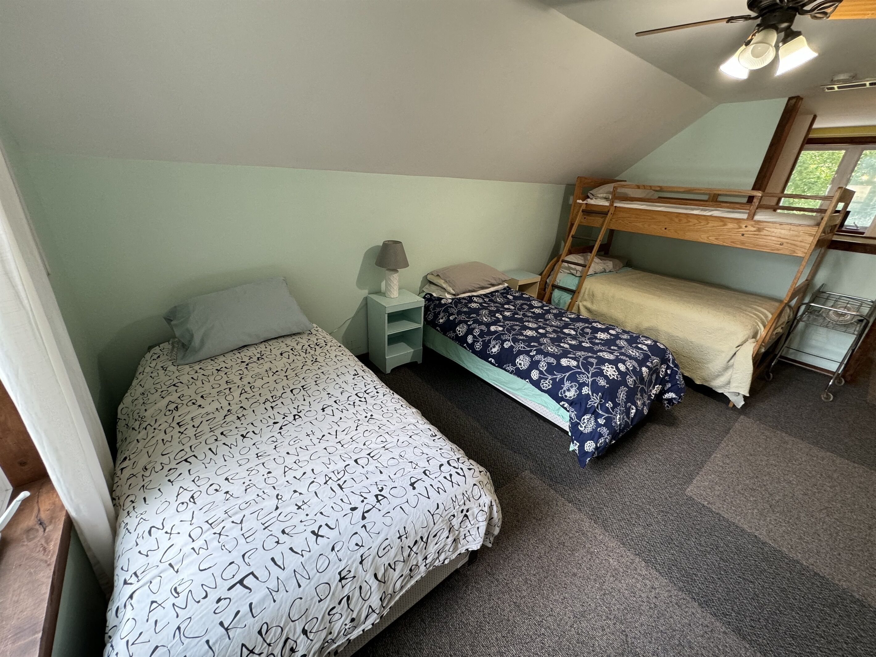 A dormitory room with bunk beds, a small desk, a lamp, and a window.
