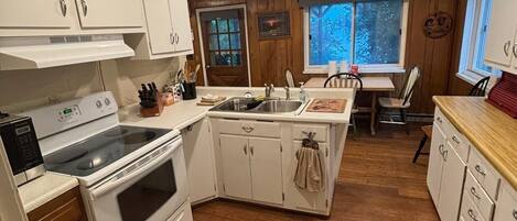 Una cocina compacta con armarios blancos, estufa y pileta.