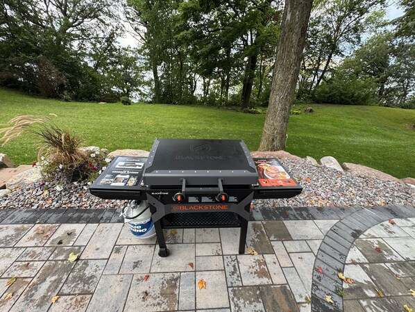 Una parrilla al aire libre con el logotipo de Blackstone, rodeada por un sendero de piedra y follaje.