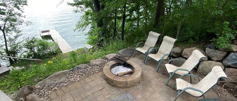 Eine Terrasse mit Feuerstelle, Sitzgelegenheiten im Freien und Blick auf einen See.