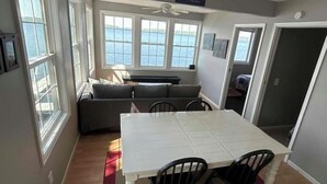 Ein Essbereich mit einem weißen Tisch und vier Stühlen, ein graues Sofa und Blick auf den See durch große Fenster.