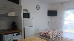 Eine kompakte Küche mit Mikrowelle, Backofen und Waschmaschine. Ein Esstisch mit Stühlen und ein an der Wand montierter Fernseher sind ebenfalls vorhanden.