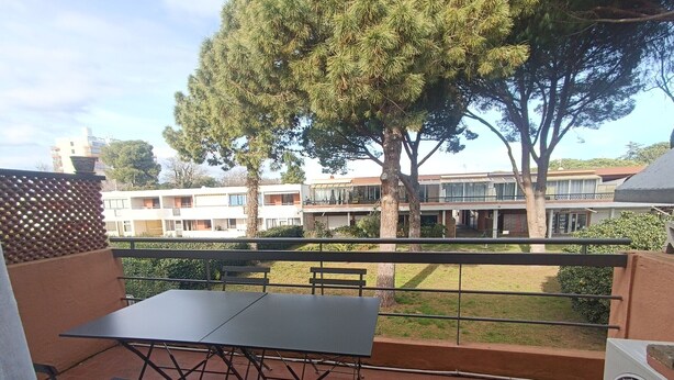 Eine Terrasse im Freien mit Tisch und Stühlen, ein großer Baum und ein Blick auf Wohnhäuser im Hintergrund.