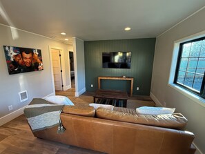 Un salon avec un canapé en cuir, un téléviseur fixé au mur et une fenêtre donnant sur un beau paysage.