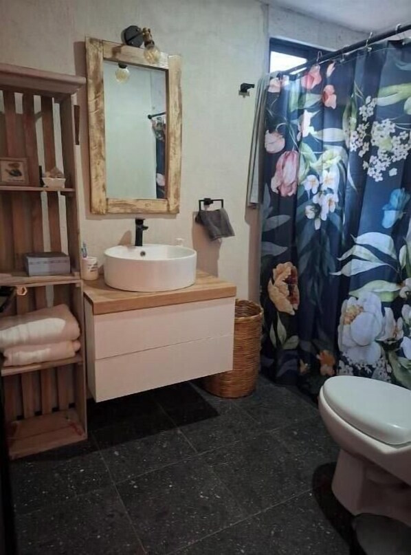 A bathroom with a wooden vanity, a white sink, a mirror, a toilet, and a floral shower curtain.
