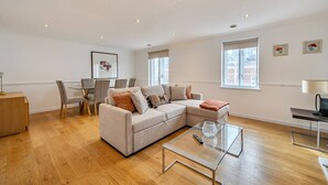 Un salon spacieux avec un grand canapé en forme de L, une table basse en verre et un coin repas comprenant des chaises et une table.