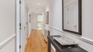 Un couloir aux murs blancs, au plancher en bois, et sur lequel se trouve une console en bois foncé agrémentée d’un objet décoratif.