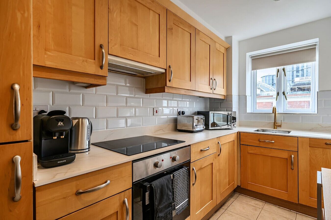 A modern kitchen with wooden cabinets, a black induction cooktop, a coffee maker, a toaster, and a microwave.