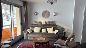 A living room with a grey sofa, patterned cushions, a round wooden coffee table, and a red patterned rug. - Gourette - Apartment 8 pers, South Balcony, Linens included, Pets allowed (Gourette)