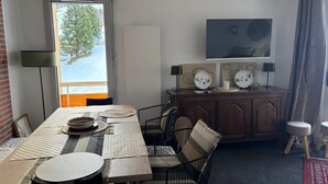 A dining area with a table set for two, a wooden cabinet with decorative plates, and a television mounted on the wall. - Gourette - Apartment 8 pers, South Balcony, Linens included, Pets allowed (Gourette)