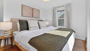 Een slaapkamer met een bed, nachtkastjes, een lamp, een raam met gordijnen en een plafondlamp.