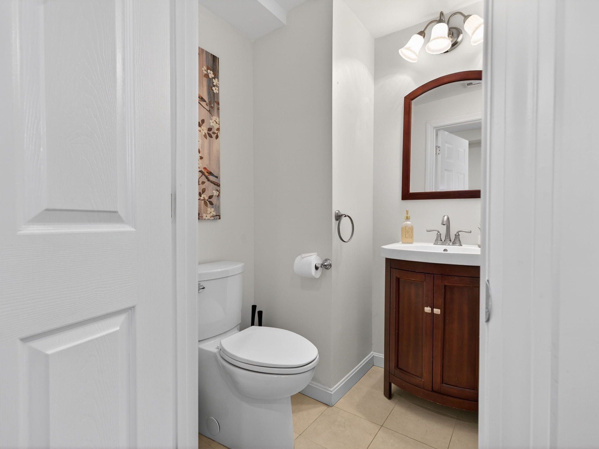 Un baño con inodoro, lavamanos, espejo y una lámpara de pared.