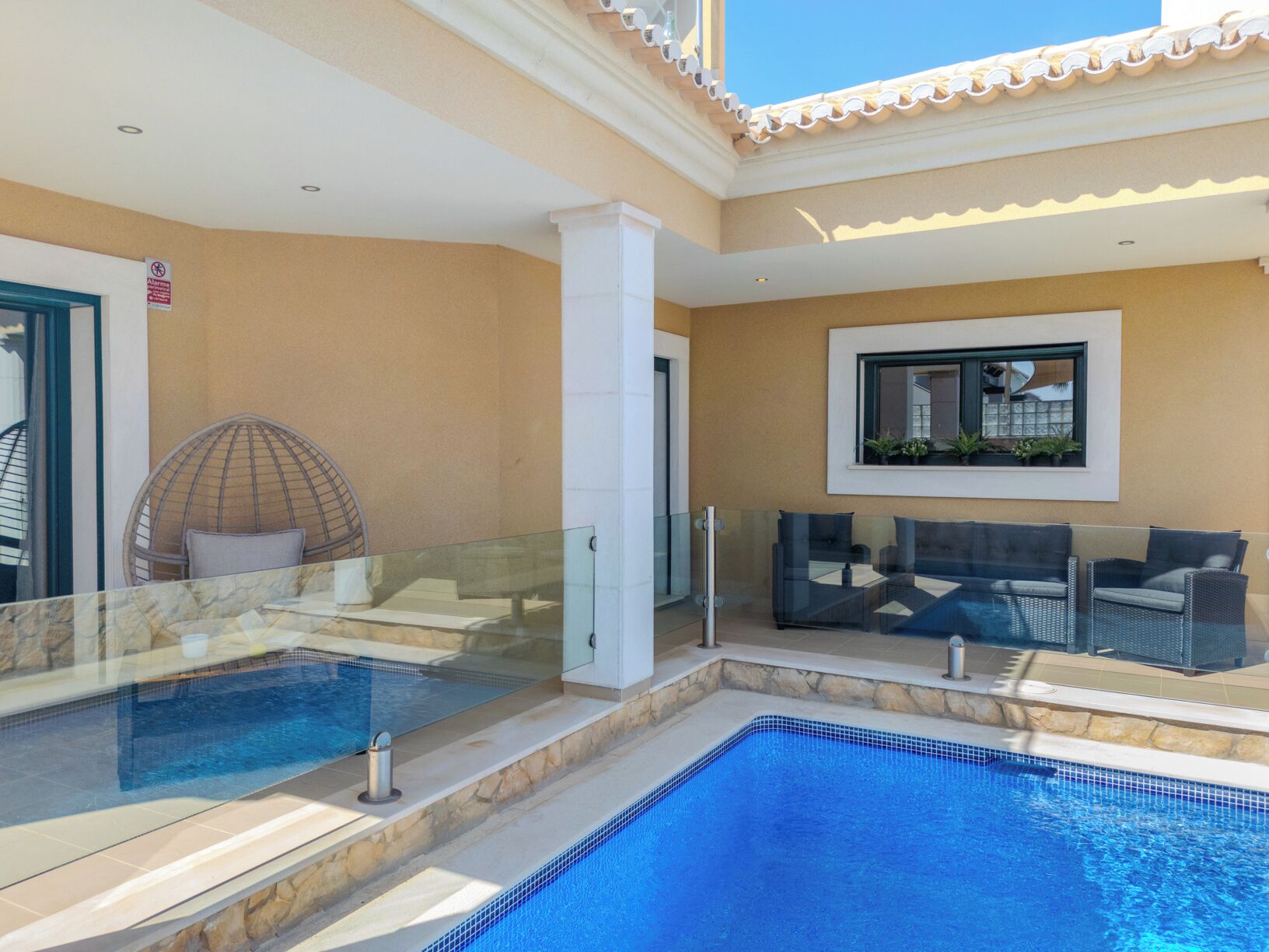Uma área de piscina com barreira de vidro, uma cadeira e um sofá.