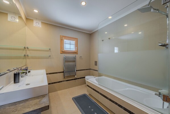 Un baño moderno con cabina de ducha de vidrio, bañera, tocador con espejo y ventana.