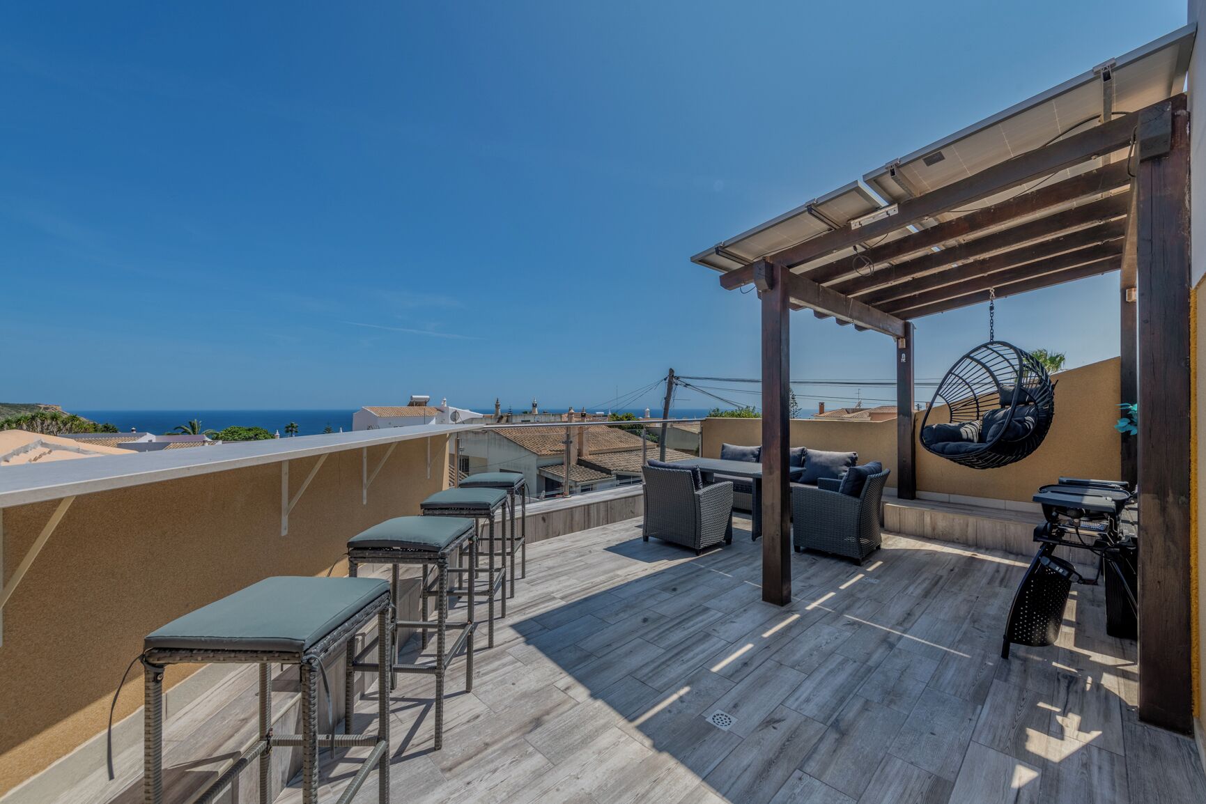 A rooftop patio with outdoor furniture, a hanging chair, and a view of the sea.