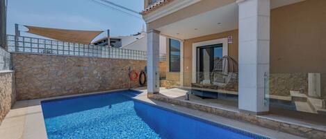 Una piscina con muros de piedra, un porche cubierto y un ventanal que da a una habitación.