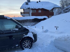 Ein mit Schnee bedecktes Auto vor einem Haus mit Holzfassade und Balkon.