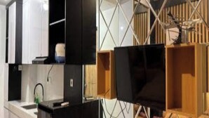 Kompakti hotellihuone, jossa on pieni keittiönurkkaus, sängynpääty ja peilillä varustettu vaatekaappi.