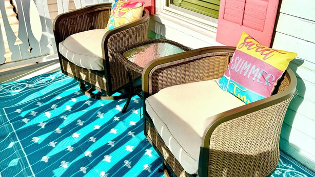 Zwei Korbstühle mit Kissen und einer blauen Matte mit Muster auf einer Veranda.
