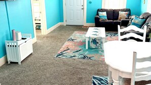 Ein Wohnzimmer mit blauer Wand, Deckenventilator, schwarzem Ledersofa, weißem Tisch und einem gemusterten Teppich.