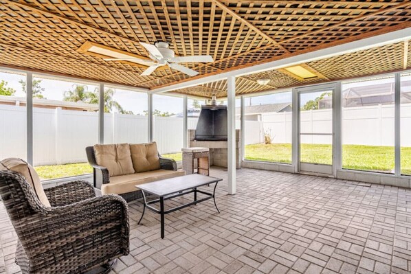 An outdoor patio with a ceiling fan, a sofa, a table, wicker chairs, and a grill.