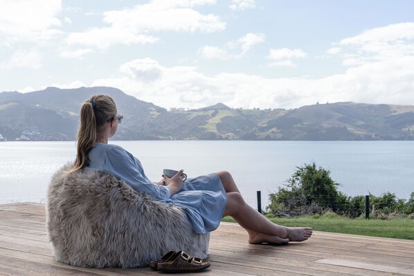 A person sitting on a wooden deck by a lake with mountains in the background.