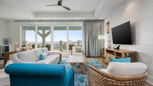 Ein geräumiges Wohnzimmer mit großem Fernseher, Deckenventilator und Blick ins Freie.