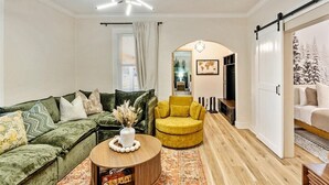 A modern living room with a green sofa, a yellow armchair, and a wooden coffee table. There is a sliding door on the right and a large window with curtains. - Hot Tub Getaway and Quiet Home Near Downtown SLC (South Salt Lake)