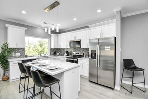 A modern kitchen with white cabinets, stainless steel appliances, and a central island with bar stools. - Enjoyable 6-bedroom house with AC in vibrant Houston (Houston)