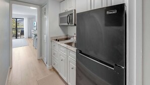 A kitchen with white cabinets, a stainless steel refrigerator, a microwave, and a sink. - Decorated 1BR Condo at Ocean Dunes Tower 1 with Pool (Myrtle Beach)