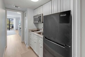 A kitchen with white cabinets, a stainless steel refrigerator, a microwave, and a sink. - Decorated 1BR Condo at Ocean Dunes Tower 1 with Pool (Myrtle Beach)