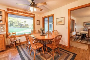 A dining room with a wooden table and chairs, a ceiling fan, and large windows with a view of a backyard. - Fabulous 6-bedroom farmhouse in charming Ririe, perfect for groups! (Ririe)