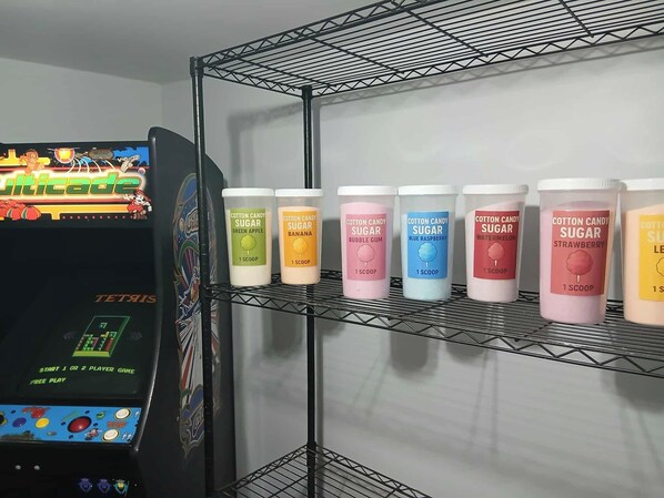 Una consola de videojuegos Tetris y un estante con recipientes de azúcar para algodón de azúcar en varios sabores.