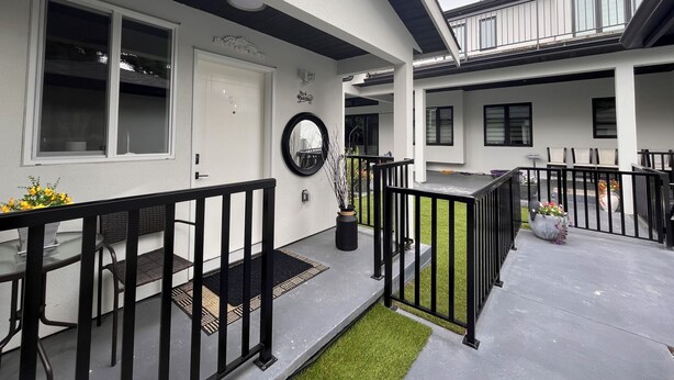 A modern building with a white exterior, black railings, and a small garden area with a bench and potted plants. - Experience 5-star comfort without the 5-star price tag. Peaceful Delta retreat  (Delta)