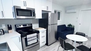 A modern kitchen with white cabinets, stainless steel appliances, and a dining area with a round table and chairs. - Experience 5-star comfort without the 5-star price tag. Peaceful Delta retreat  (Delta)