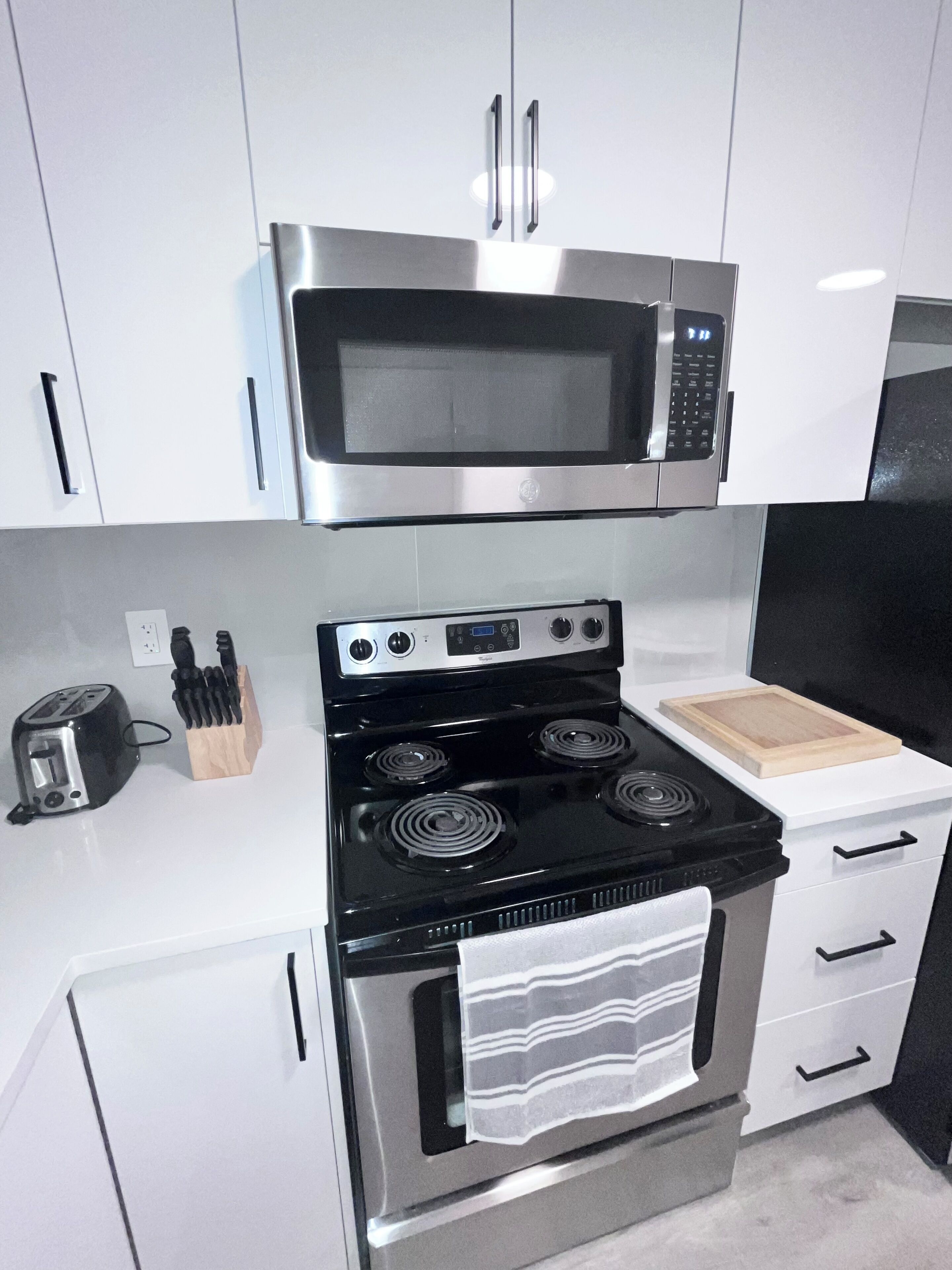 A kitchen with white cabinets, a stainless steel microwave, a black stove, and a toaster.