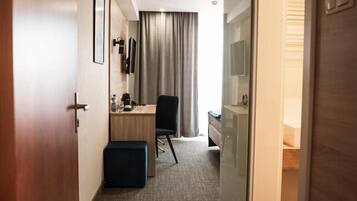 A hotel room with a desk, chair, and a bed.
