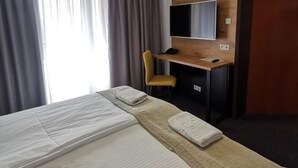A hotel room with a bed, a desk with a TV, a chair, and a wooden panel wall. - Gold Hotel Zlotoryja (Zlotoryja)