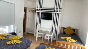 Quarto com duas camas, uma escrivaninha e uma televisão.