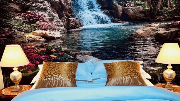 Ein Bett mit Blick auf einen Wasserfall, zwei Lampen und Kissen mit Muster.