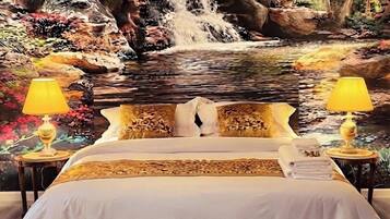 A bed with a white bedspread, two bedside lamps, and a view of a waterfall and foliage.