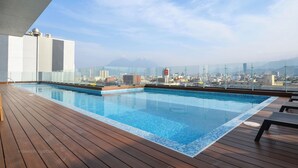 Ein Pool auf dem Dach mit Blick auf die Stadt, einer Holzterrasse und einer Glasbrüstung.