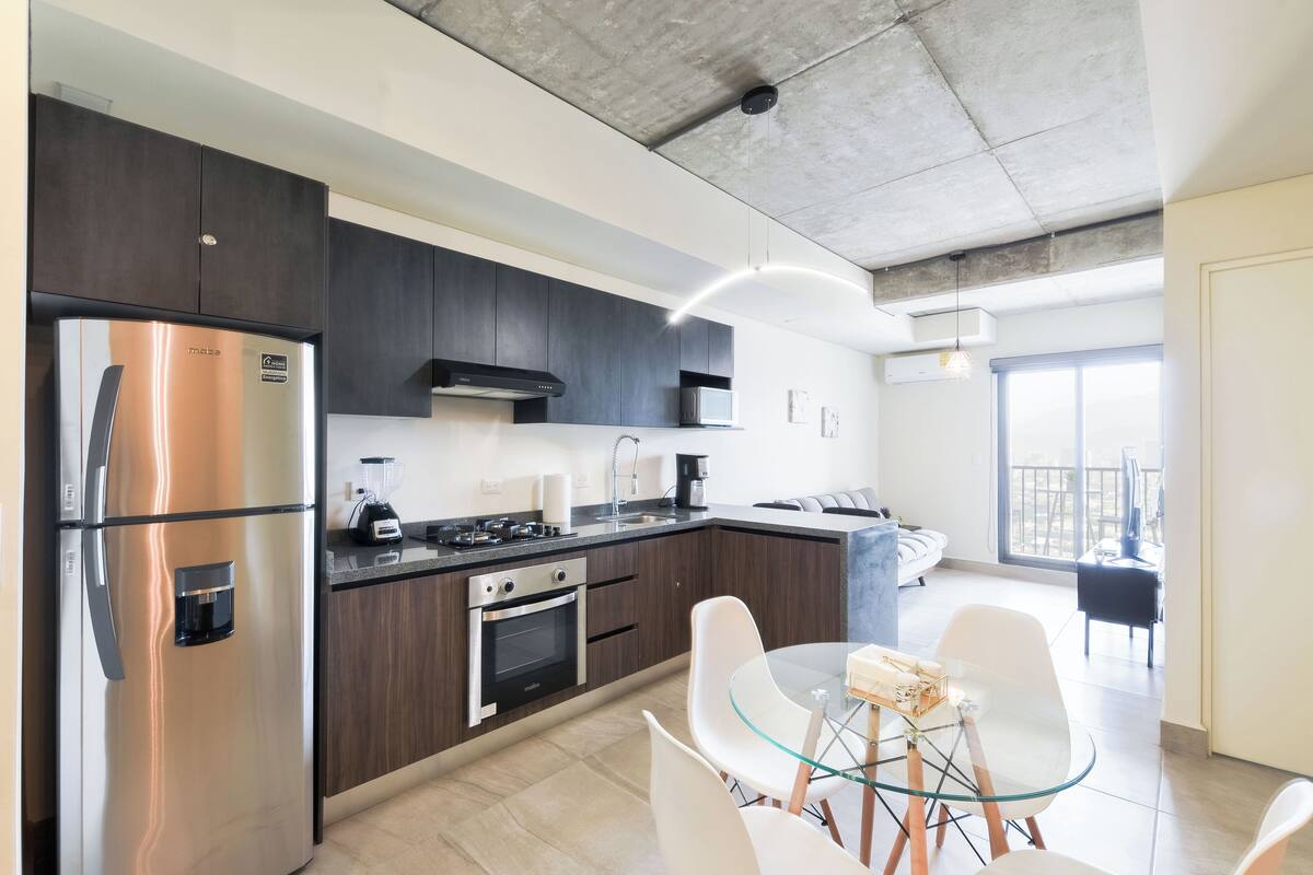 A modern kitchen with stainless steel appliances, dark cabinetry, and a glass dining table.