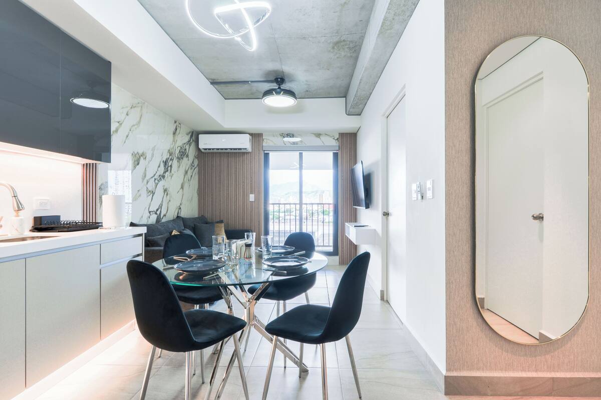 A modern kitchen with a marble backsplash, a dining area with a glass table and black chairs, and a large mirror on the wall.