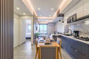 Una cuina moderna amb zona de menjador, que inclou una illa central, electrodomèstics integrats i una finestra gran que deixa entrar llum natural.