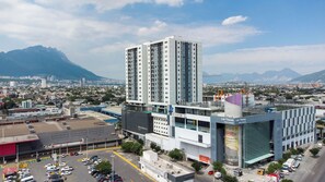 Un edifici alt amb nombrosos pisos, envoltat d'un paisatge urbà i muntanyes al fons.