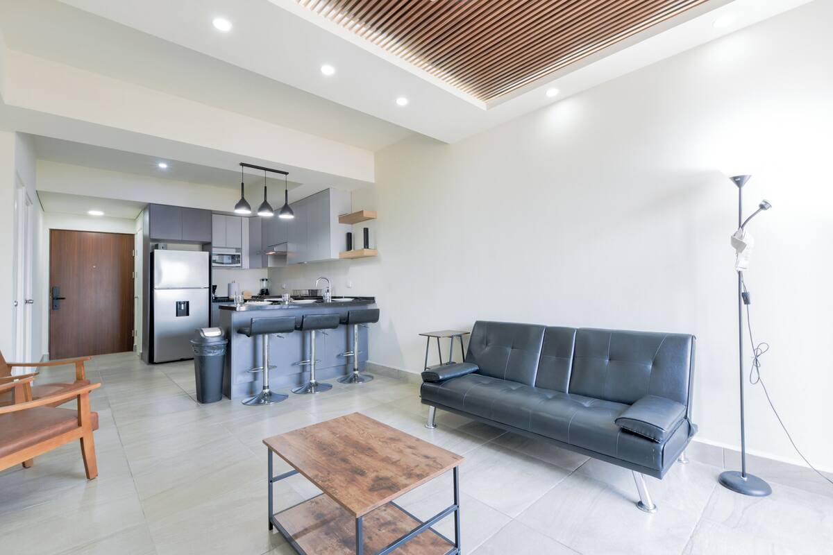 A modern living room with a sofa, a coffee table, and a kitchen in the background.