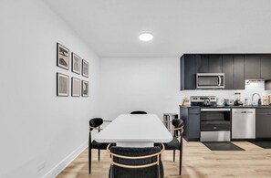 Een moderne keuken met een wit aanrecht, roestvrijstalen apparatuur en een zwarte achterwand.